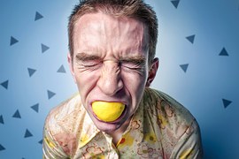 Homem com péssima expressão facial enquanto come um limão, mostrando que comer pode ser uma tortura.